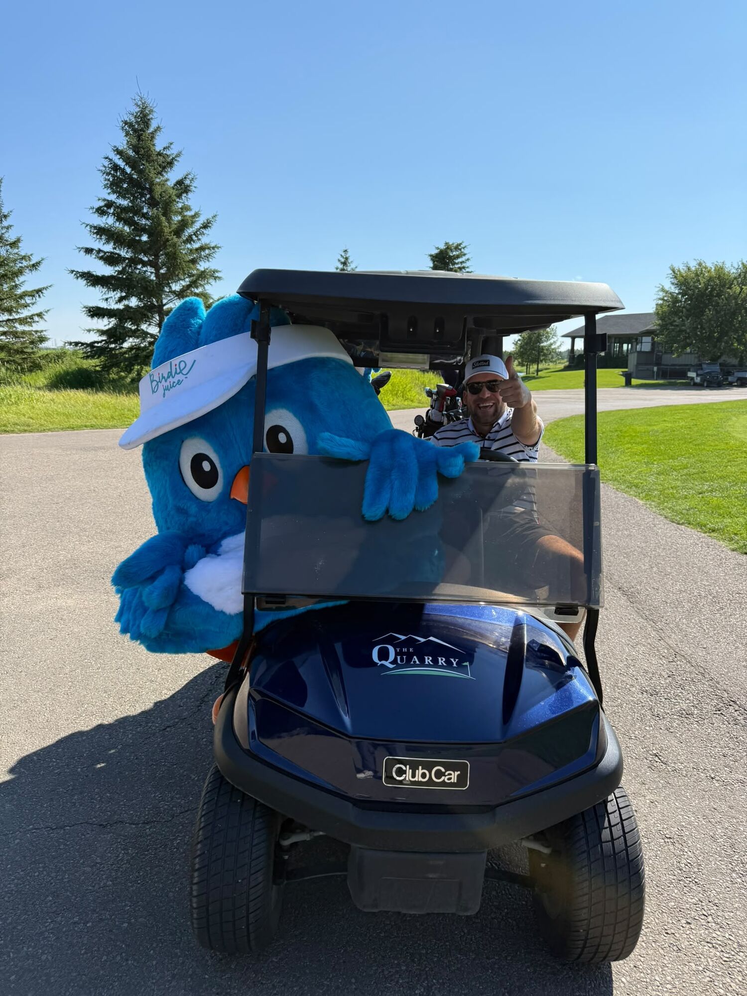 The Birdie Juice mascot riding shotgun in a golf cart at The Quarry while the driver gives a thumbs up