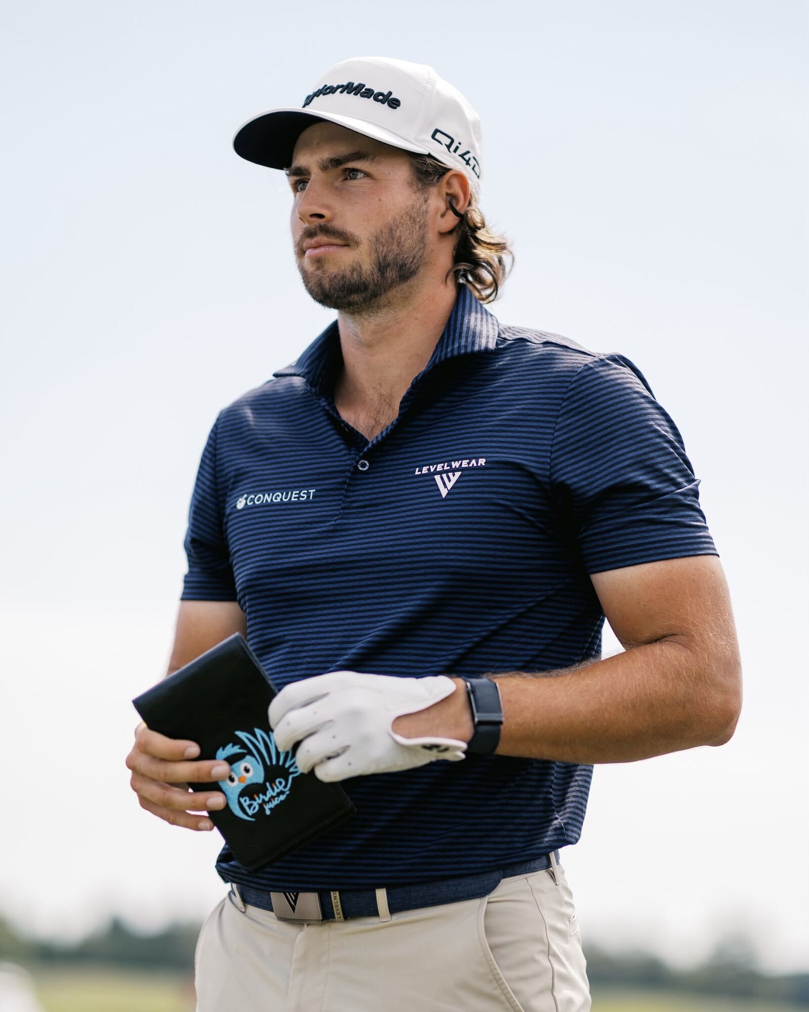 A golfer in a navy polo and white cap walking the fairway, holding a Birdie Juice yardage book