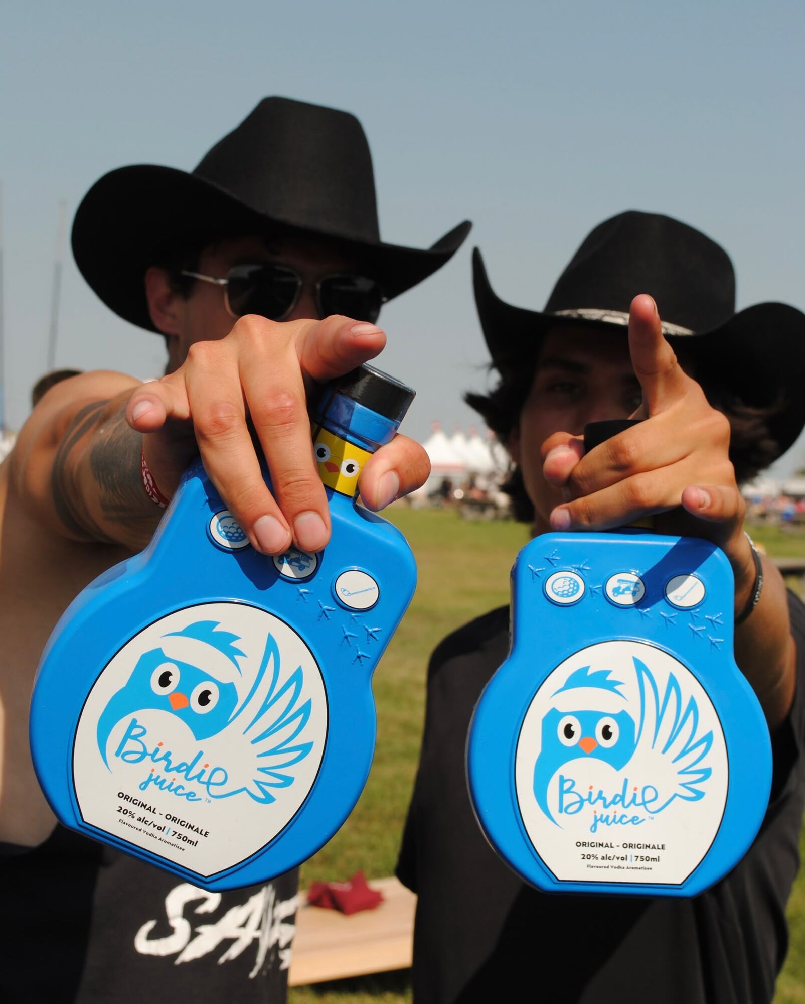 Two festival-goers in black cowboy hats holding Birdie Juice bottles out towards the camera